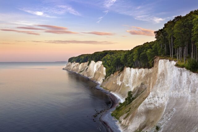 KI-ANWENDUNG Eine Küstenlandschaft mit weißen Kreidefelsen entlang der Küstenlinie der Ostsee in Rügen und einem dichten Buchenwald im Nationalpark Jasmund darüber.