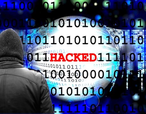 Warum Cyberangriffe auf Reisebüros zielen Cyberangriff auf Reisebüros: Ein Mann im Mantel und ein Monitor mit dem roten Titel „Hacker“ sowie verschiedene Daten im Hintergrund symbolisieren einen Cyberangrifdfd von einem Hacker