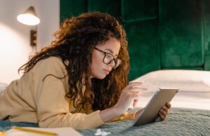 Welche Kriterien die Hotelwahl beeinflussen Kriterien für die Hotelwahl: Frau mit Brille liegt bäuchlings auf einem Bett im Laptop