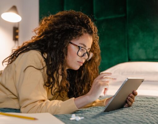 Welche Kriterien die Hotelwahl beeinflussen Kriterien für die Hotelwahl: Frau mit Brille liegt bäuchlings auf einem Bett im Laptop