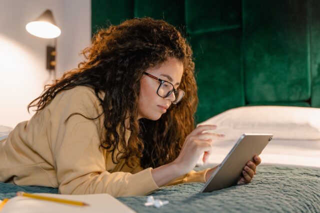 Entscheidende Kriterien bei der Hotelwahl Kriterien für die Hotelwahl: Frau mit Brille liegt bäuchlings auf einem Bett im Laptop
